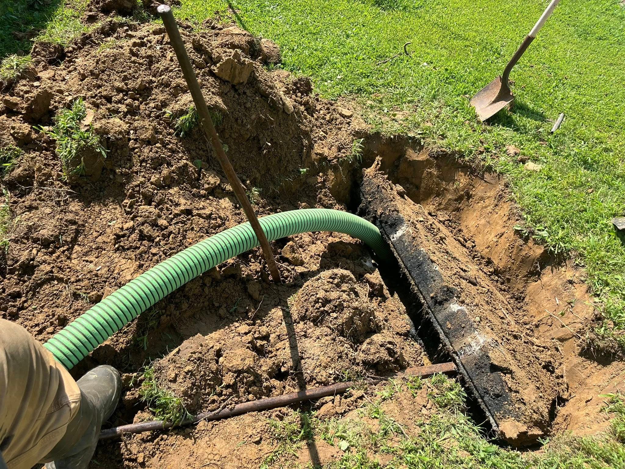 Septic tank pumping in progress with green hose going into excavated tank