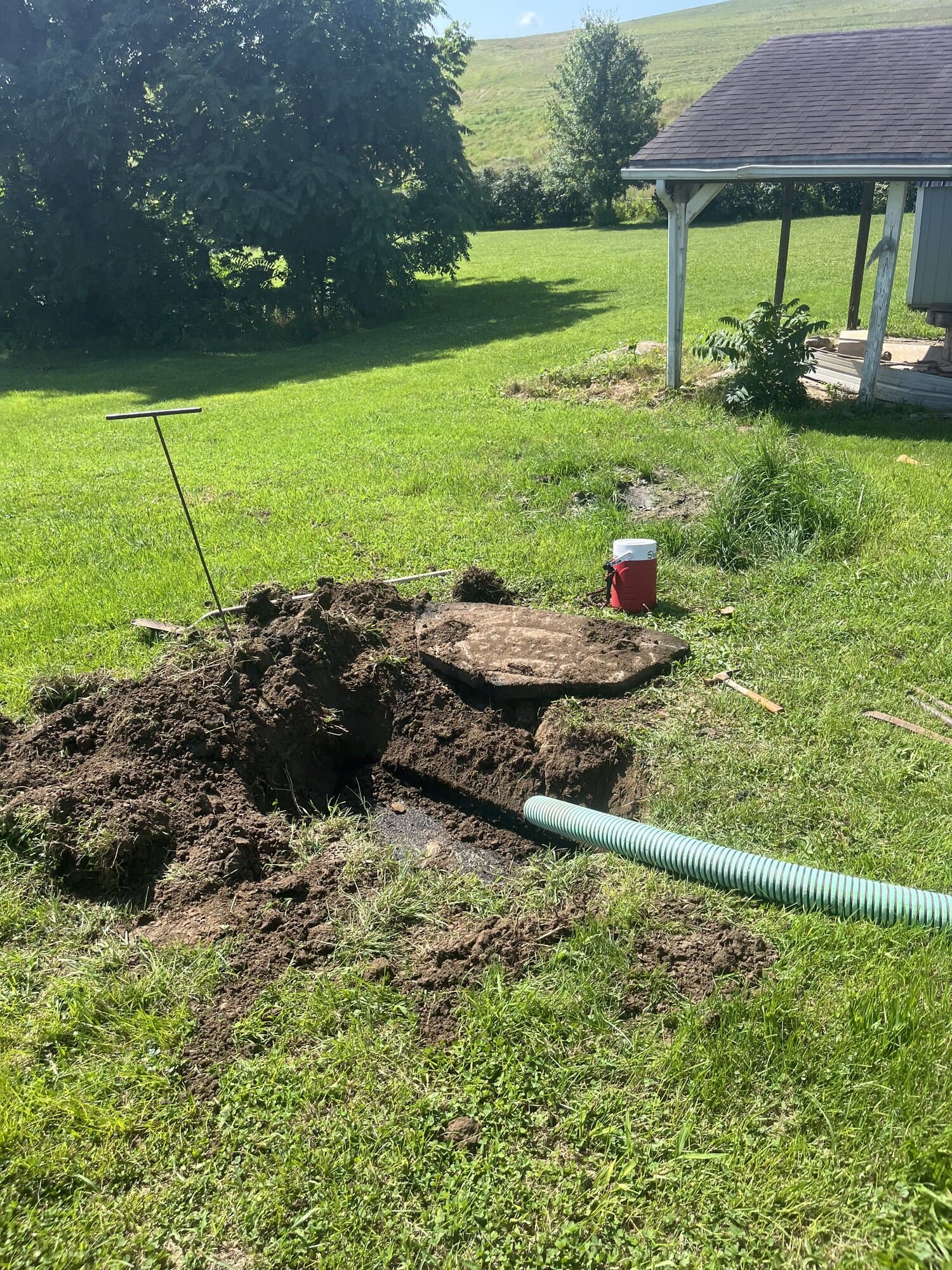 Excavated septic tank with pump hose during a tank locating and pumping job